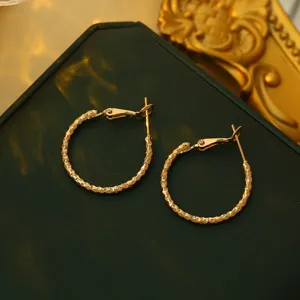 Detailopname van gestructureerde gouden creolen oorbellen op donker, chic accessoire.