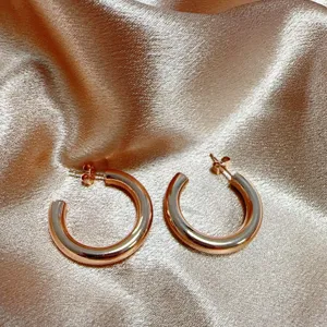 Detailopname van stijlvolle grove rosé-gouden oorbellen met een slank hol design.