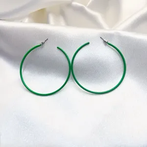 Detail van grote groene metalen gelakte oorbellen met een gladde afwerking en stijlvol design.