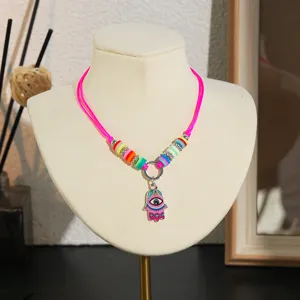 Gedetailleerd opname van kleurrijke kleikralen ketting met hamsa hand hanger voor kids.