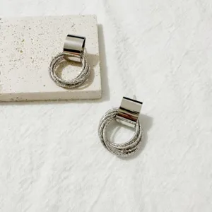 Detailopname van meercirkelige zilveren oorbellen met textuurringen en gladde metalen top.