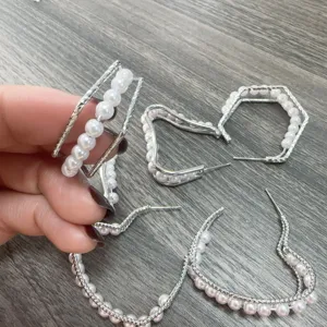 Detailopname van geometrische oorbellen met parels en zilverkleurig multistraal ontwerp.