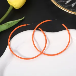 Detail van opvallende oranje metalen oorringen met een glanzende snoepkleur afwerking.