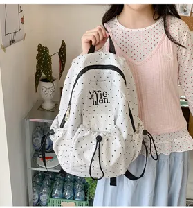 Detail shot of a stylish white polka dot backpack with front drawstring pocket and zipper.