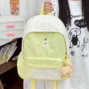 Gros plan du sac à dos jaune à carreaux avec broderie de pomme et charmant pendentif en peluche.