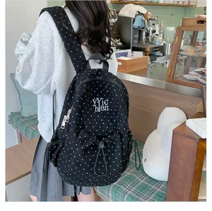 Detail view of stylish black canvas backpack with white polka dots, zipper and front pocket.