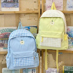 Vue détaillée du sac à dos à carreaux doux avec charmante broderie de pomme et poche avant.