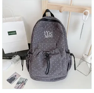 Grey polka dot canvas backpack detail view showcasing front drawstring pocket and zipper.