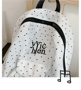 Close-up detail of a white canvas backpack with black polka dots, black zipper and front pocket.