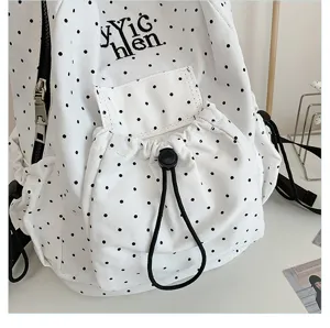 Close-up detail of white canvas backpack featuring black polka dots and black drawstring pocket.
