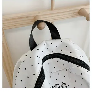 Close-up detail of a white canvas backpack with classic black polka dots and zipper.
