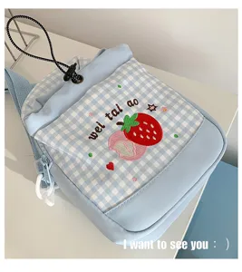 Detailfoto van lichtblauwe geruite studentenrugzak met schattige aardbeiborduursel en trekkoord.