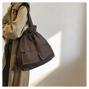 Detail view of the brown plaid drawstring tooling backpack, showing strap and fabric texture.
