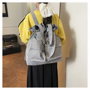 Detail view of grey plaid canvas drawstring backpack, utilitarian fashion rucksack with pockets.