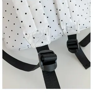 Detailed view of white polka dot backpack shoulder strap and black adjustable plastic buckle.