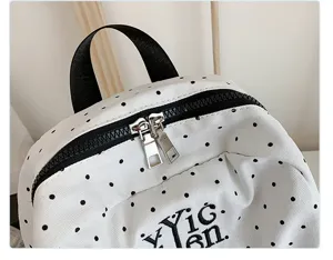 Close-up detail of white polka dot canvas backpack with black zipper and top handle.