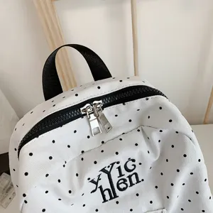 Casual white polka dot backpack with black handle, stylish canvas school bag for daily commute.