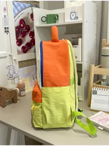 Side detail view of a colorful student backpack featuring orange and green color-block design.
