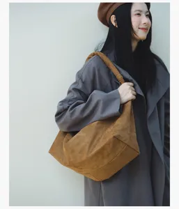 Detailed shot of a brown suede slouchy shoulder bag worn by a model, casual retro style.