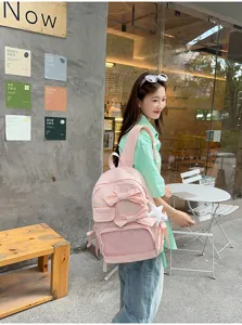 Vista detallada de la mochila rosa con lazo y bolsillo frontal transparente en cafetería.