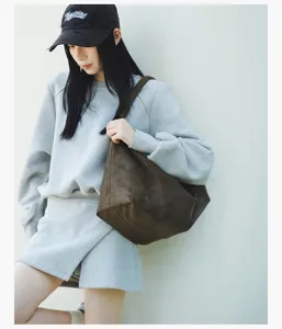 Detailed view of the stylish brown vintage shoulder bag worn by a model in casual grey outfit.