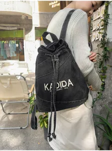 Vintage washed denim backpack detail showing drawstring closure and embroidered logo design.