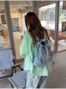 Details of the vintage washed denim backpack showing its drawstring closure and casual street style.