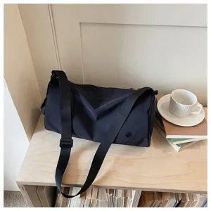 Détail de sac bandoulière cylindrique en nylon noir sur bureau en bois avec livres et tasse.