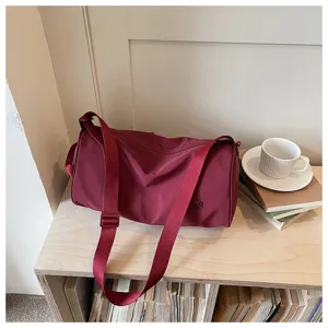 Vue détaillée du sac bandoulière cylindrique en nylon rouge foncé dans la scène.
