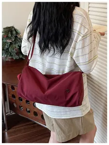 Sac bandoulière en nylon décontracté avec détail du design cylindrique rouge foncé.
