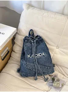 Close-up detail of a vintage washed denim drawstring backpack with embroidered letter logo on soft cushion.