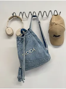 Detailed view of the washed vintage denim backpack hanging with hat and headphones on wall hook.