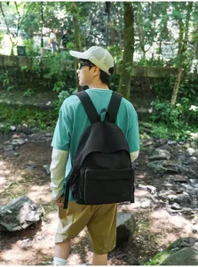 Vue rapprochée du sac à dos de voyage noir, porté par un modèle dans un magnifique cadre boisé.