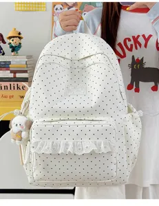 Gedetailleerd overzicht van schattige witte rugzak met polkadots, kanten volant en pluche hanger.