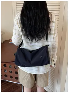 Vue détaillée d'un sac porté épaule cylindrique en nylon noir sur un mannequin décontracté.