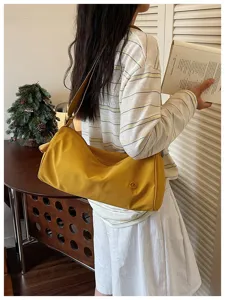 Détail de sac porté épaule cylindrique en nylon jaune, sac besace décontracté avec logo en métal.
