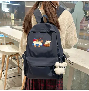 Stylish navy blue school backpack detail featuring cute cartoon embroidery and a plush pendant.
