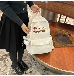 Detailed view of the white canvas school backpack featuring cute puppy embroidery and plush charm.