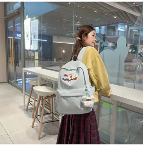 Detailed scene showing the light blue canvas school backpack with cute embroidery patch and charm.