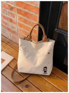 Détail du sac cabas en toile avec tissu texturé, poignées marron et poche avant.