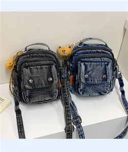 Denim cross-body bag detail showing washed texture, multi-pocket design, and cute bear pendant.