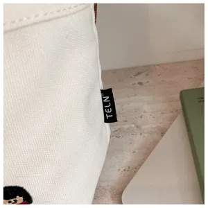 Gros plan de détail sur un sac à main en toile blanche avec étiquette latérale de marque.