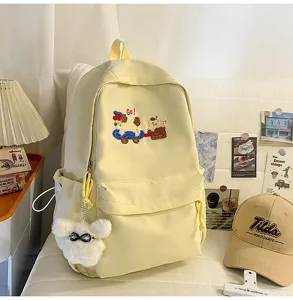 Detailed view of a light yellow canvas backpack featuring cute puppy embroidery and fluffy bear charm.