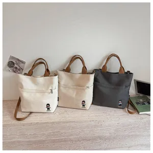 Vue détaillée du sac cabas décontracté en toile avec poche avant, double poignée et bandoulière.