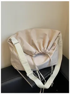 Gros plan détaillé du sac bandoulière beige à cordon montrant la texture du tissu et la large sangle.
