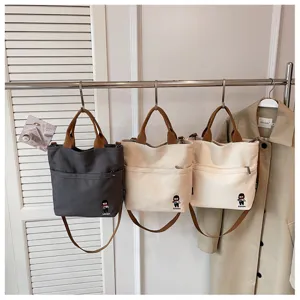 Détail du sac à bandoulière en toile avec tissu résistant et poche avant pratique.