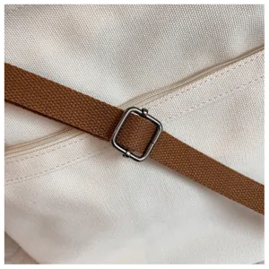 Gros plan de détail du sac bandoulière en toile montrant la sangle marron et la boucle métallique.