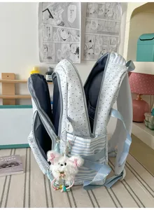 Gedetailleerd aanzicht van lichtblauwe stippenrugzak met pluche hanger en gestreepte zakken.