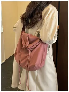 Gros plan sur le sac besace rose à cordon, montrant un tissu souple et des lanières.