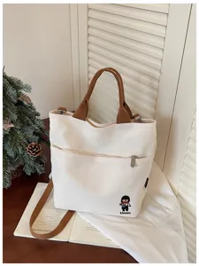 Sac bandoulière en toile avec anses marron, poche zippée avant et broderie délicate.